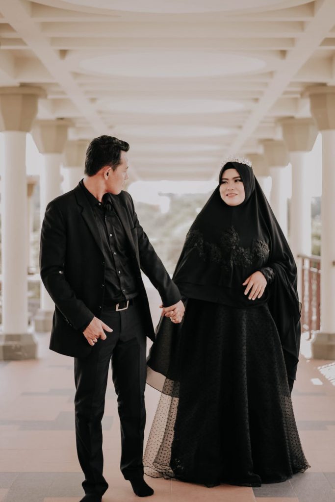 man in black suit holding hands with woman wearing black hijab