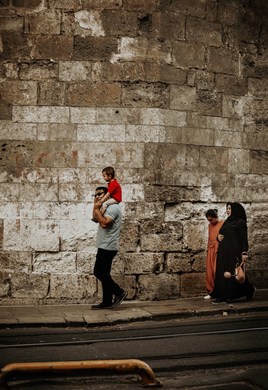 muslim family walking on pathway near old shabby wall