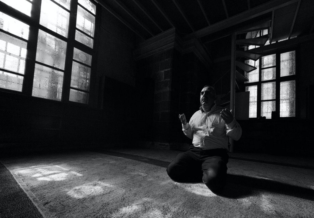 anonymous ethnic man praying on knees in temple
