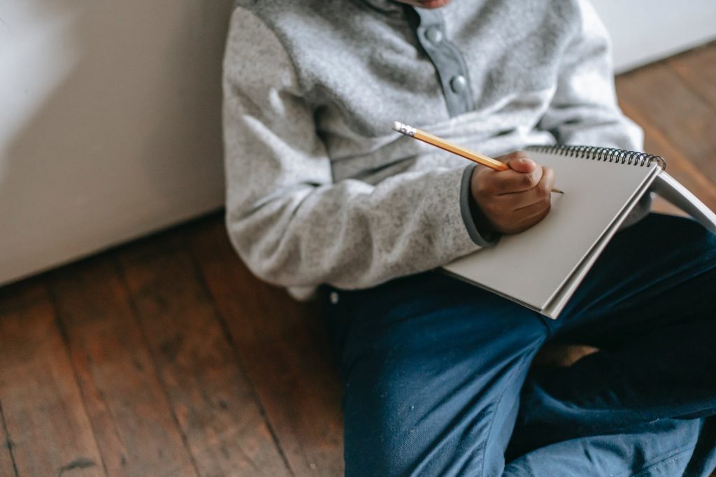crop ethnic schoolkid writing in notepad